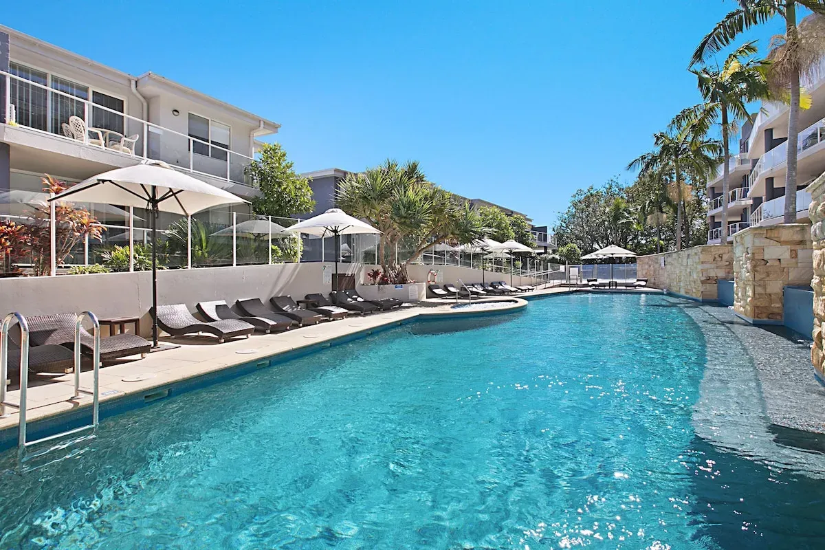 Pool surrounded by apartment balconies and palms at Mantra Nelson Bay